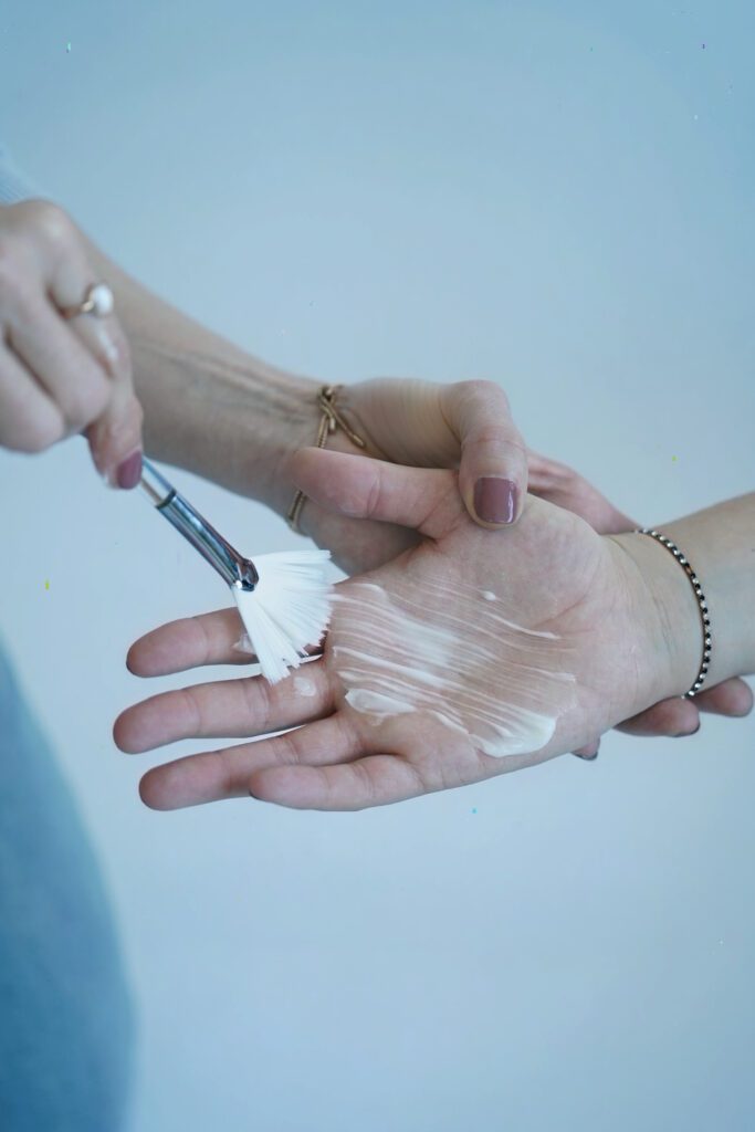 Creme wird mit einem Fächerpinsel auf eine Handfläche aufgetragen