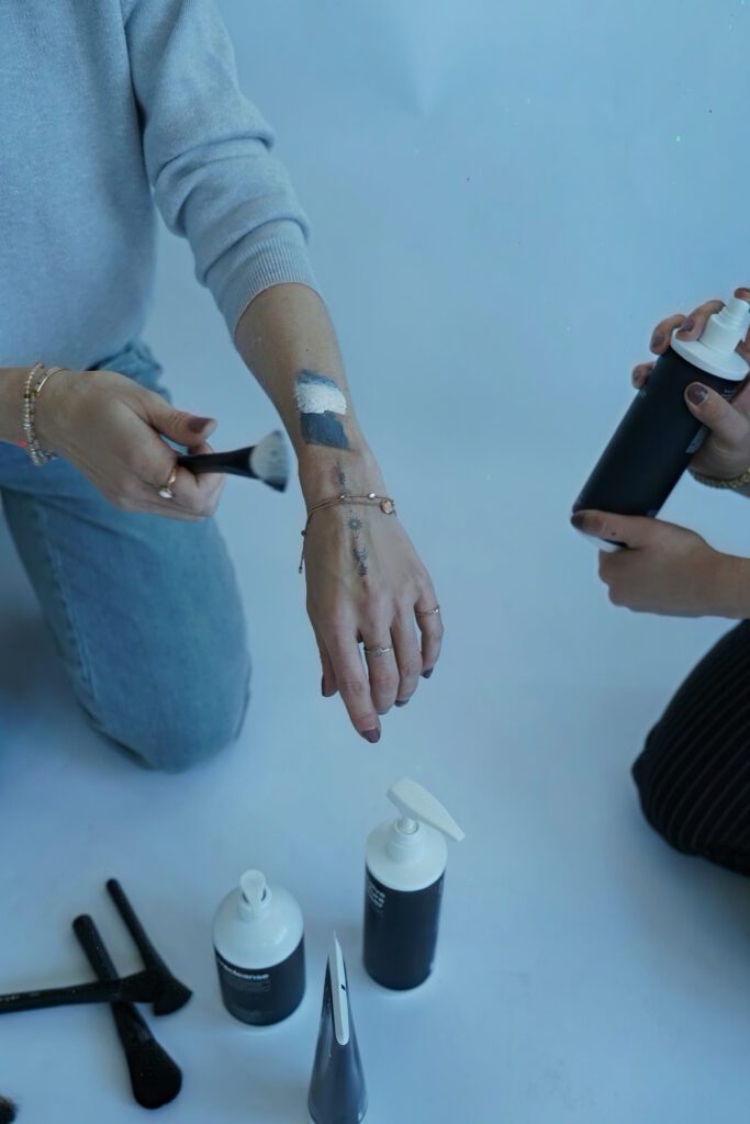 Zwei Personen tragen Make-up auf den Unterarm auf, daneben Pflegeprodukte und Pinsel